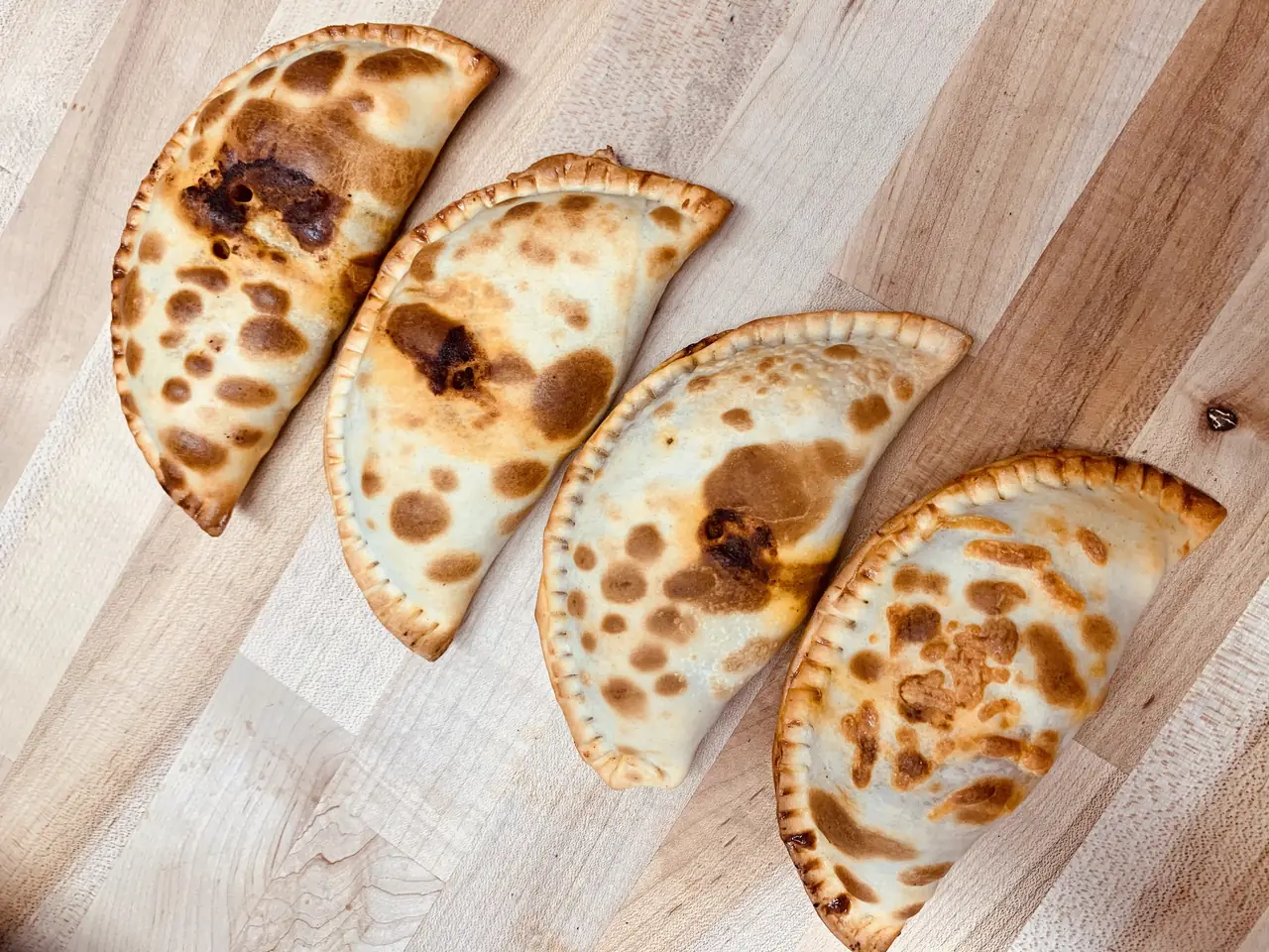 Four baked empanadas in a row on a wooden board