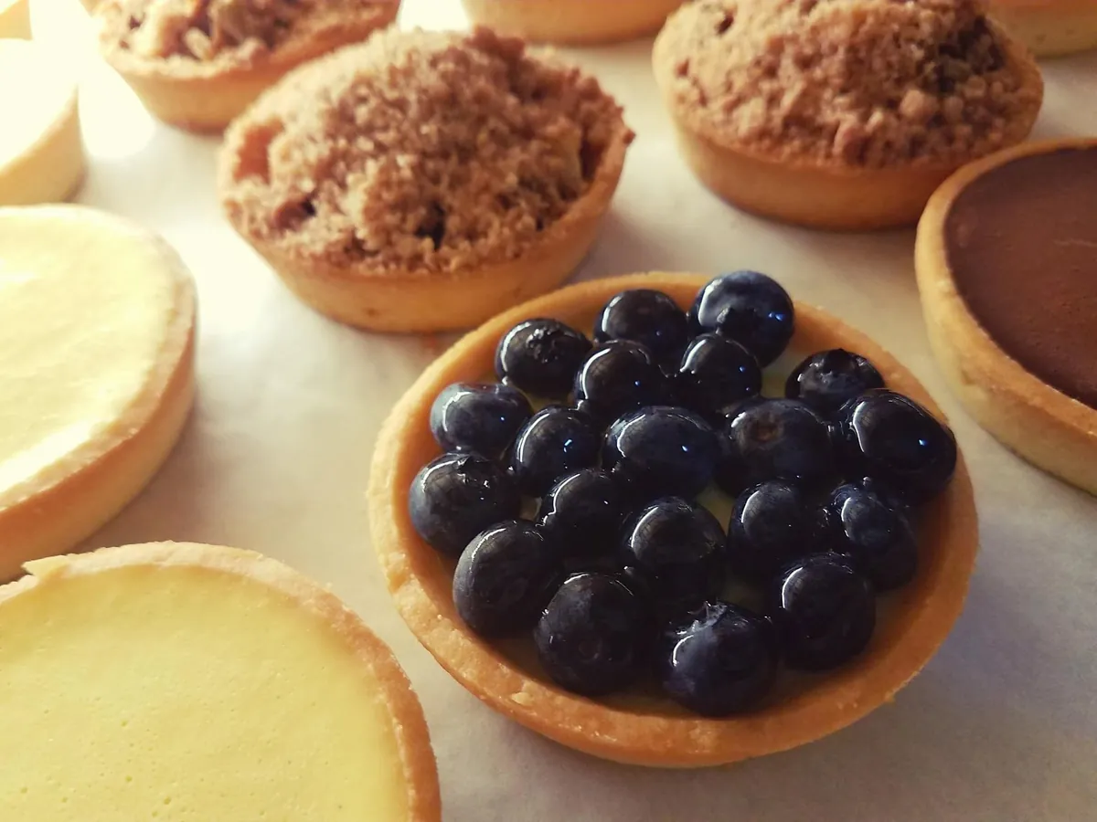 Assorted sweet tarts on parchment, with a blueberry tart in front